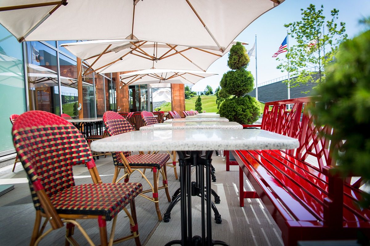 Outdoor dining area with red chairs and marble tables under large umbrellas.