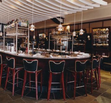 Elegant bar with curved counter and stylish chairs under hanging lights.