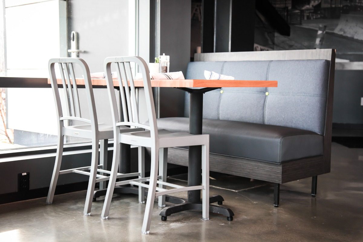 Minimalist dining area with metal chairs and a wooden table near a gray cushioned bench.