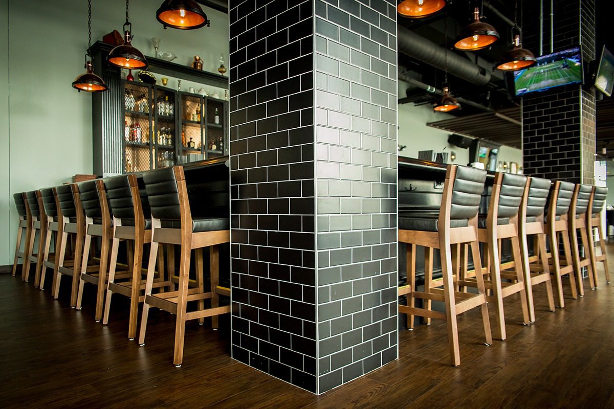 Modern bar interior with black tiled pillar and wooden stools.