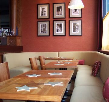 Cozy restaurant corner with wooden tables and framed photos on a red wall.
