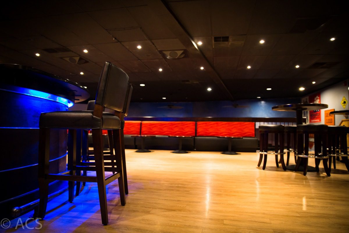 Empty bar area with wooden floors and red cushioned seating.