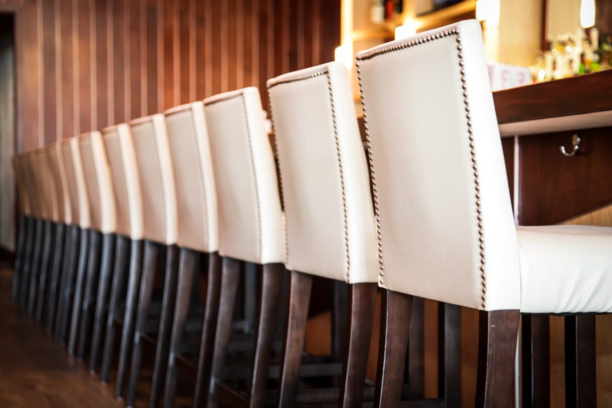 Row of elegant white bar stools with nailhead trim in a cozy setting.