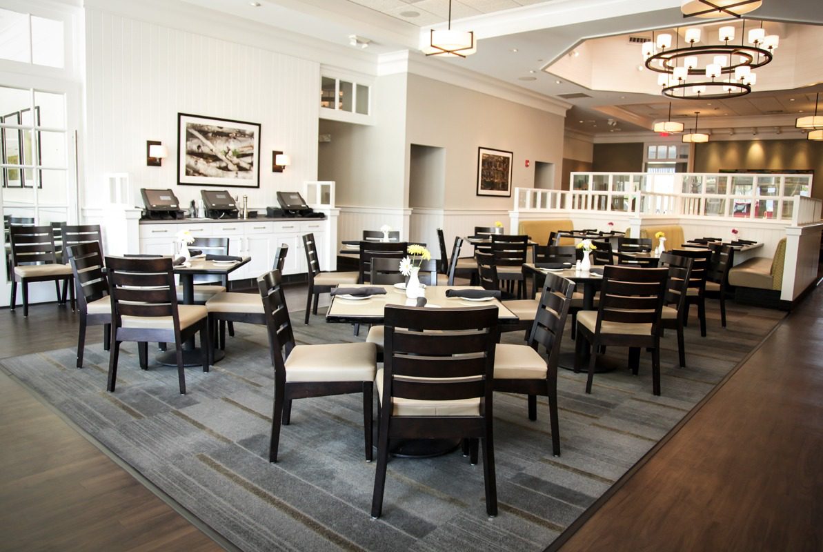 Empty dining area with dark wooden chairs and tables in a bright room.