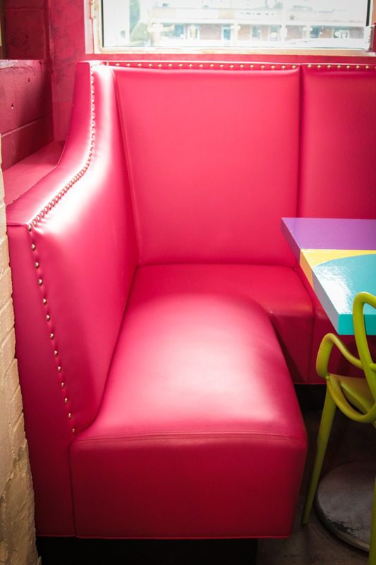 Bright pink cushioned booth seating with a corner table and colorful chairs.
