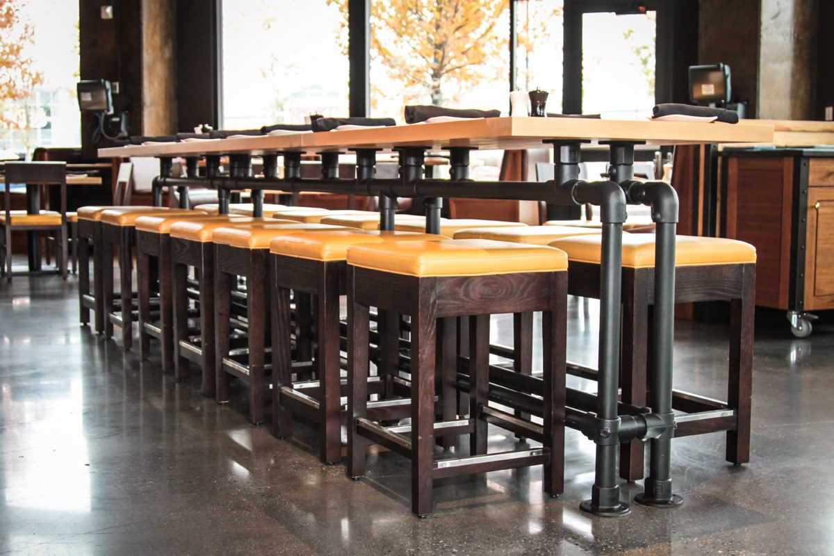 Row of wooden stools lined up at a bar counter with natural light.