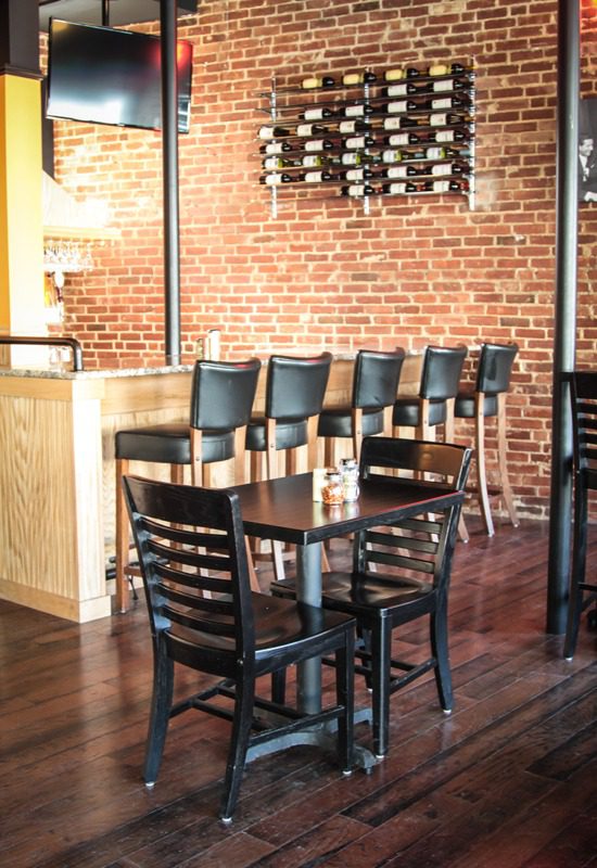 Cozy brick-walled cafe with wooden tables and black chairs.