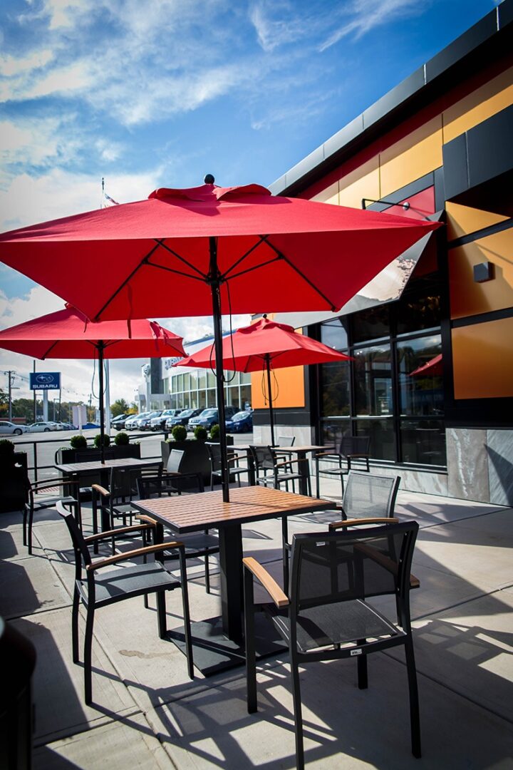 Outdoor seating area with red umbrellas and black chairs on a sunny day.