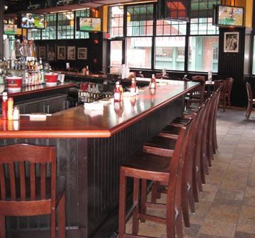 Empty bar with wooden stools and large windows.