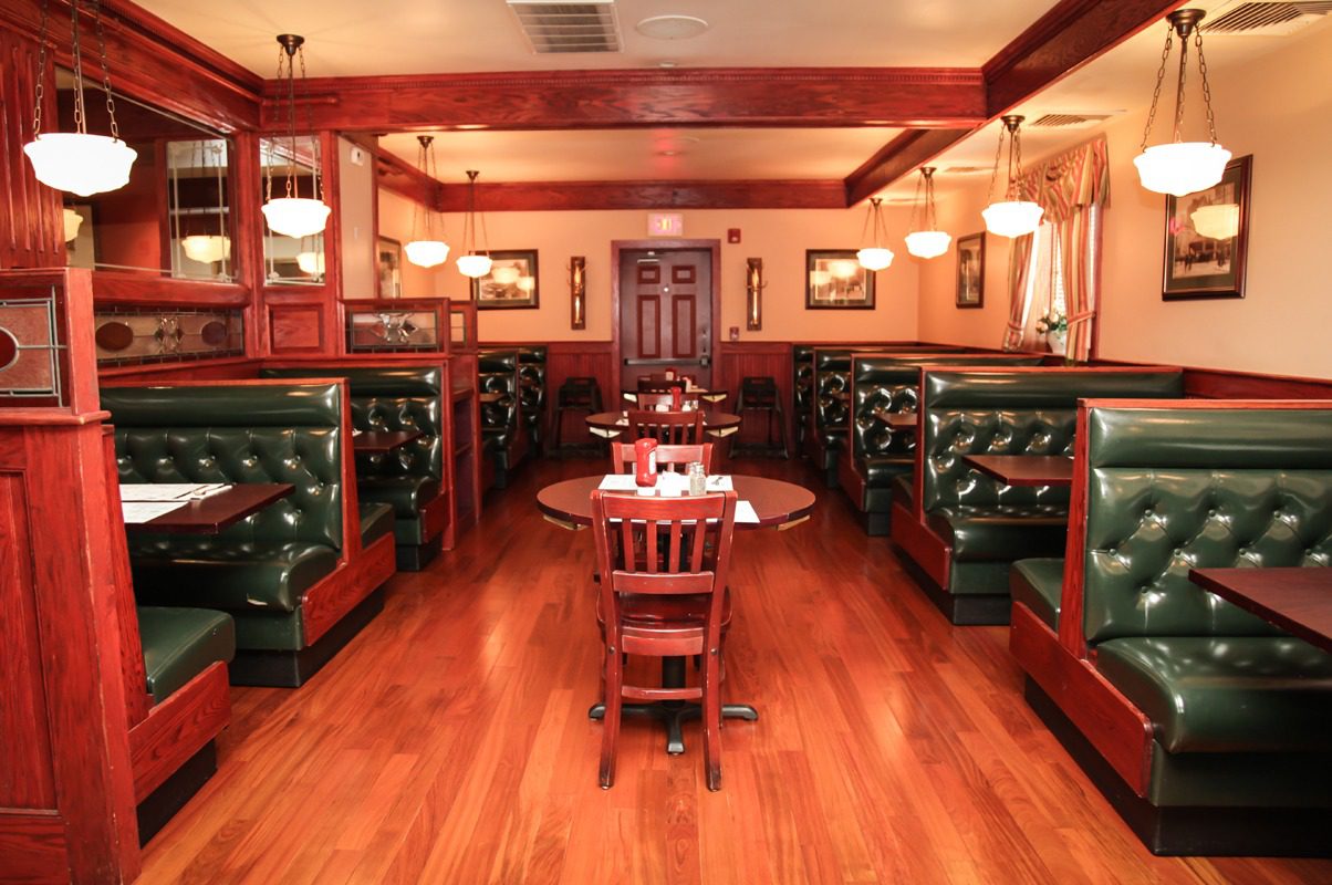 Cozy vintage-style restaurant interior with wooden floors and green leather booths.