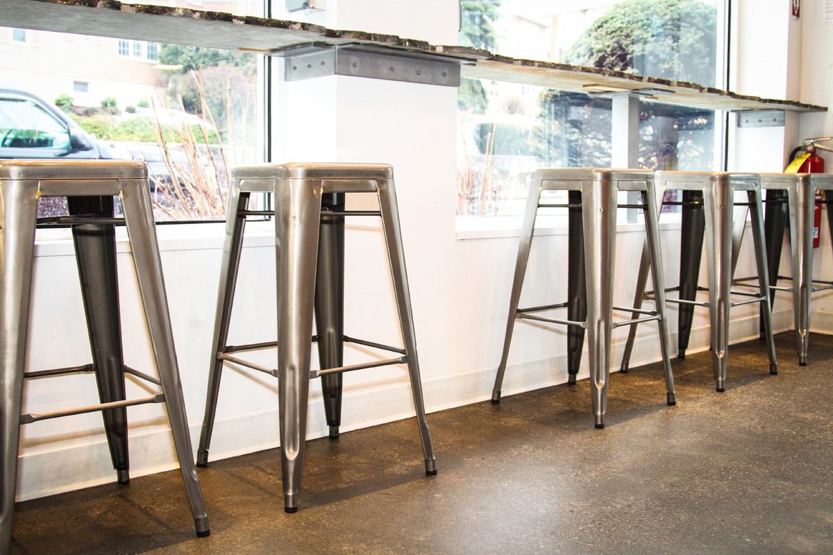 Metal bar stools with wooden seats lined up beside a bright window.