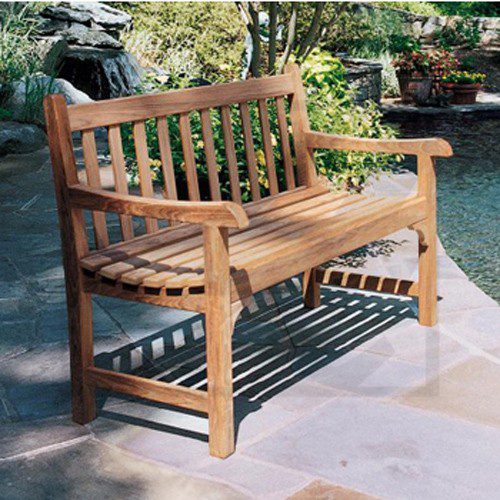 A wooden bench on a patio with garden greenery in the background.
