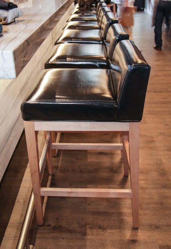 Black leather bar stools with wooden legs lined up on a wooden floor.
