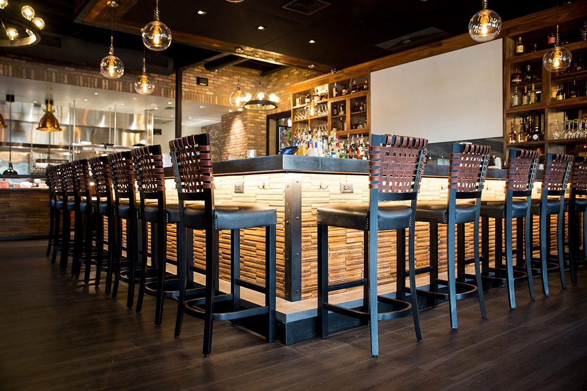 Modern bar with wooden stools and warm lighting.