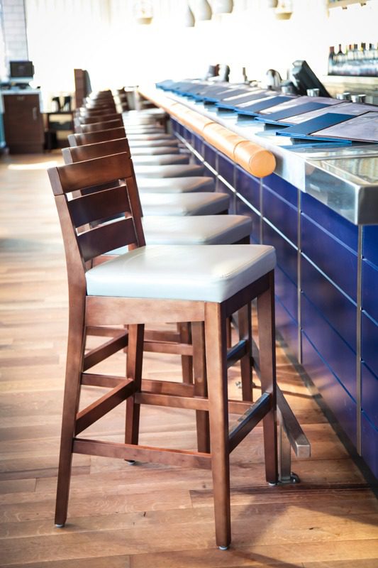 Row of wooden bar stools with white cushions along a blue tiled bar counter.