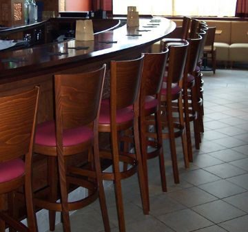 A row of wooden bar stools with red cushions along a bar counter.