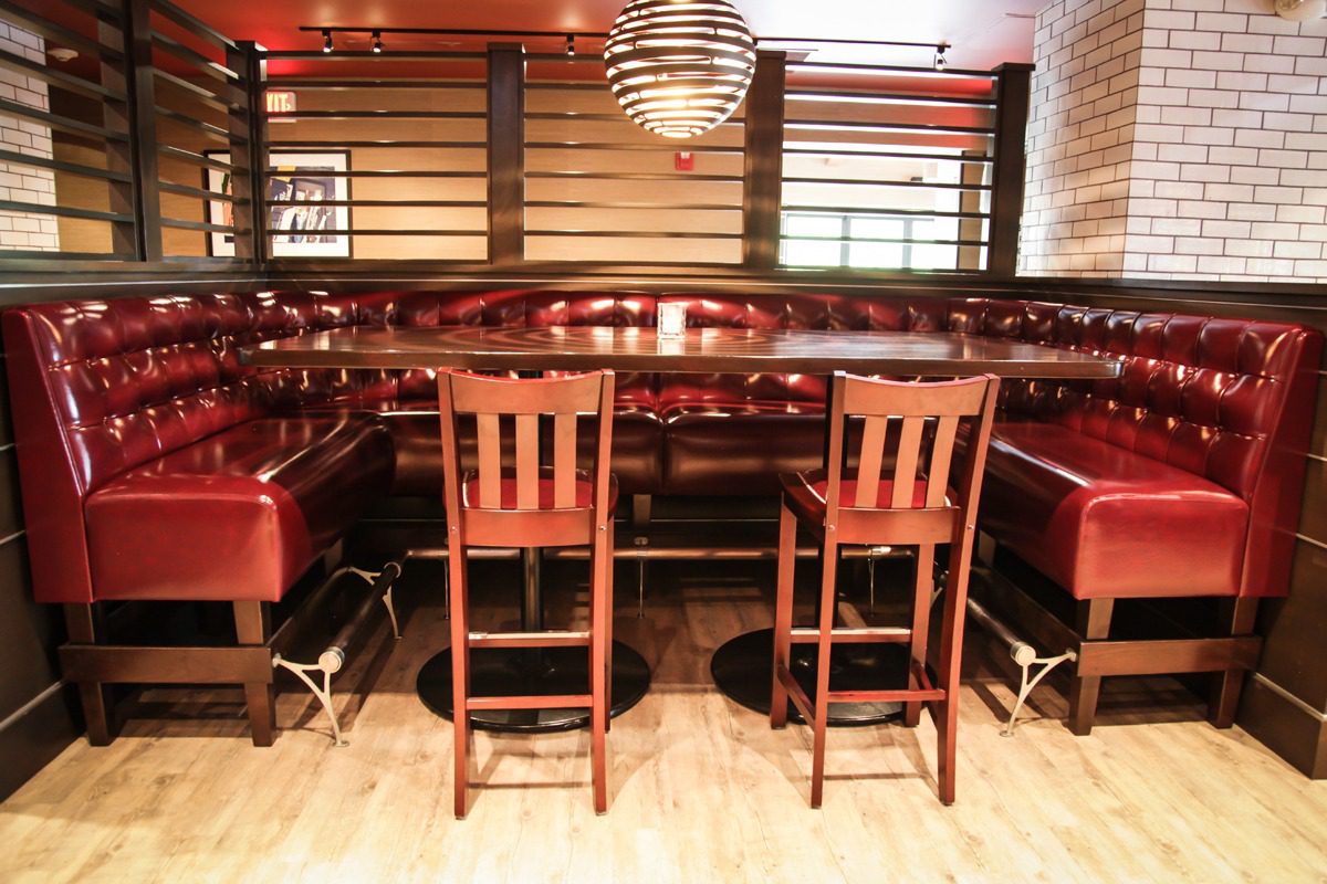 Cozy red leather booth with wooden chairs in a warmly lit restaurant.