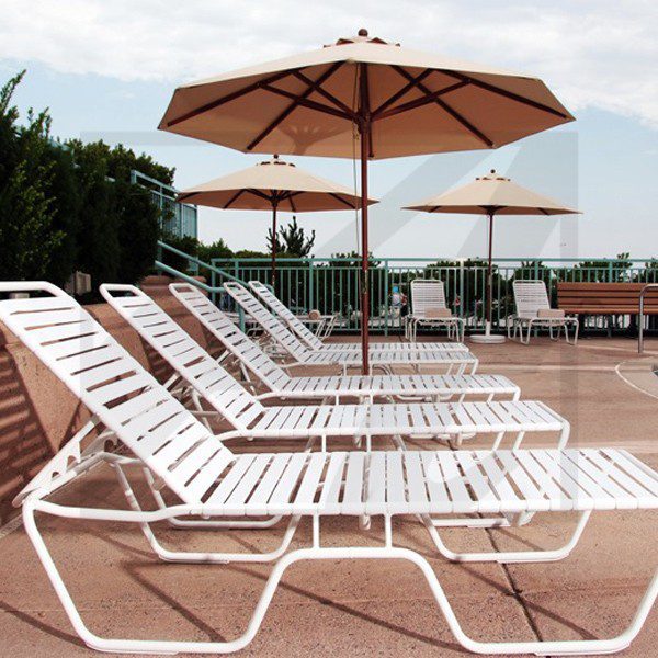 Empty white lounge chairs with umbrellas on a sunny poolside patio.