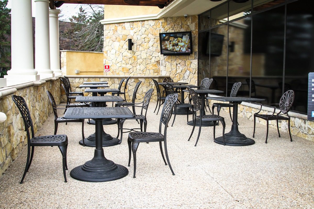 Empty outdoor cafe seating area with black metal chairs and tables.