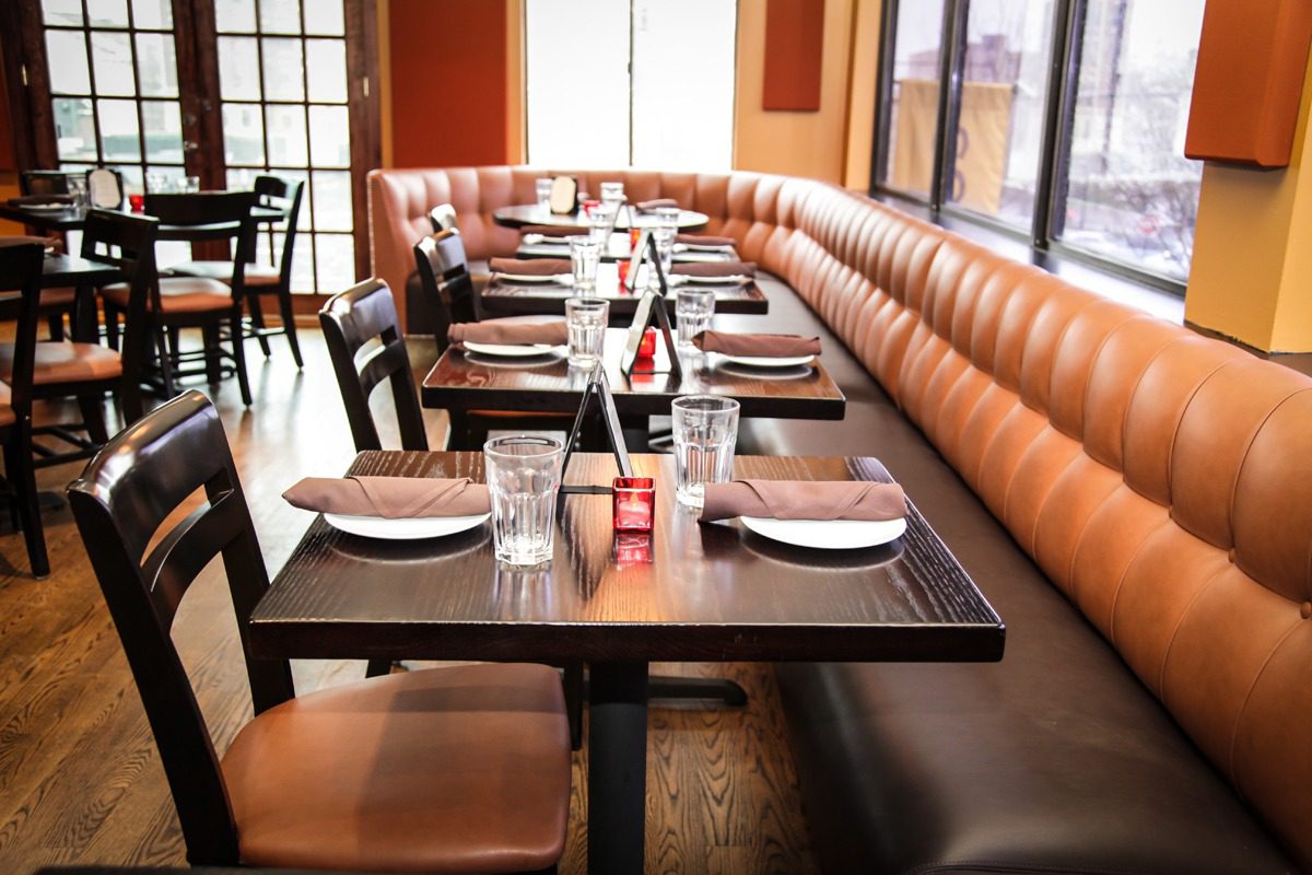 Cozy restaurant seating with neatly set tables and leather banquettes.