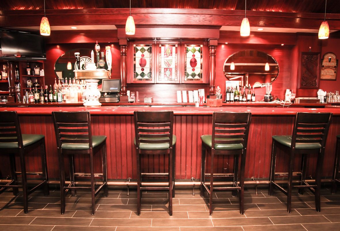 Cozy wooden bar with four high stools and warm lighting.