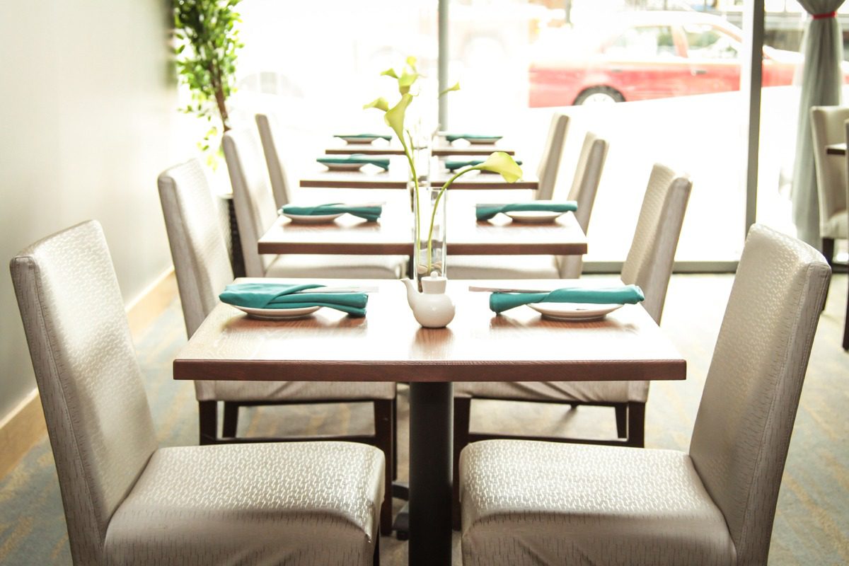 Elegant dining tables neatly set with teal napkins and flower vases.
