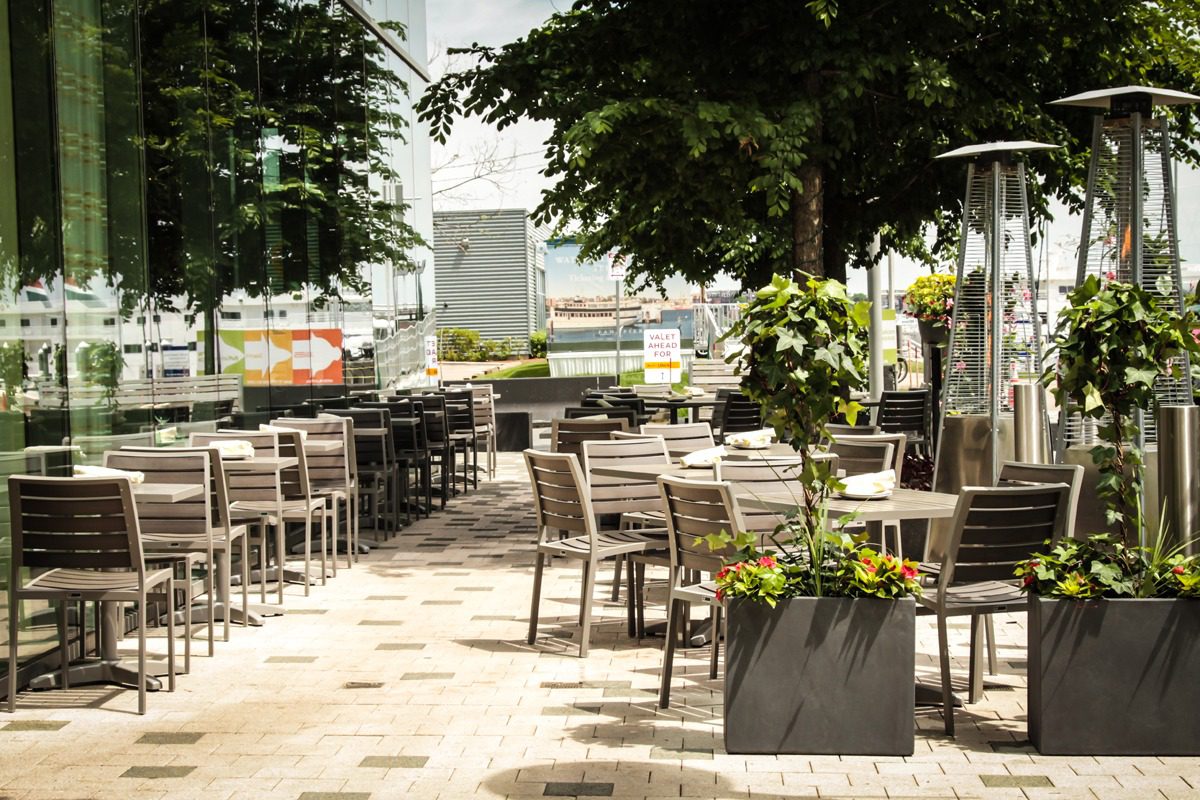 Empty outdoor café seating area under shade trees on a sunny day.