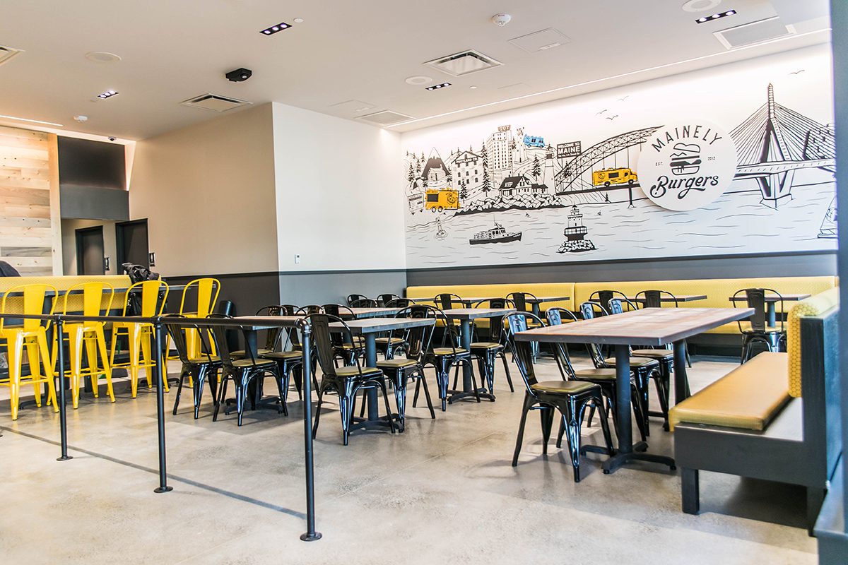 Modern cafeteria with yellow and black chairs and cityscape wall art.