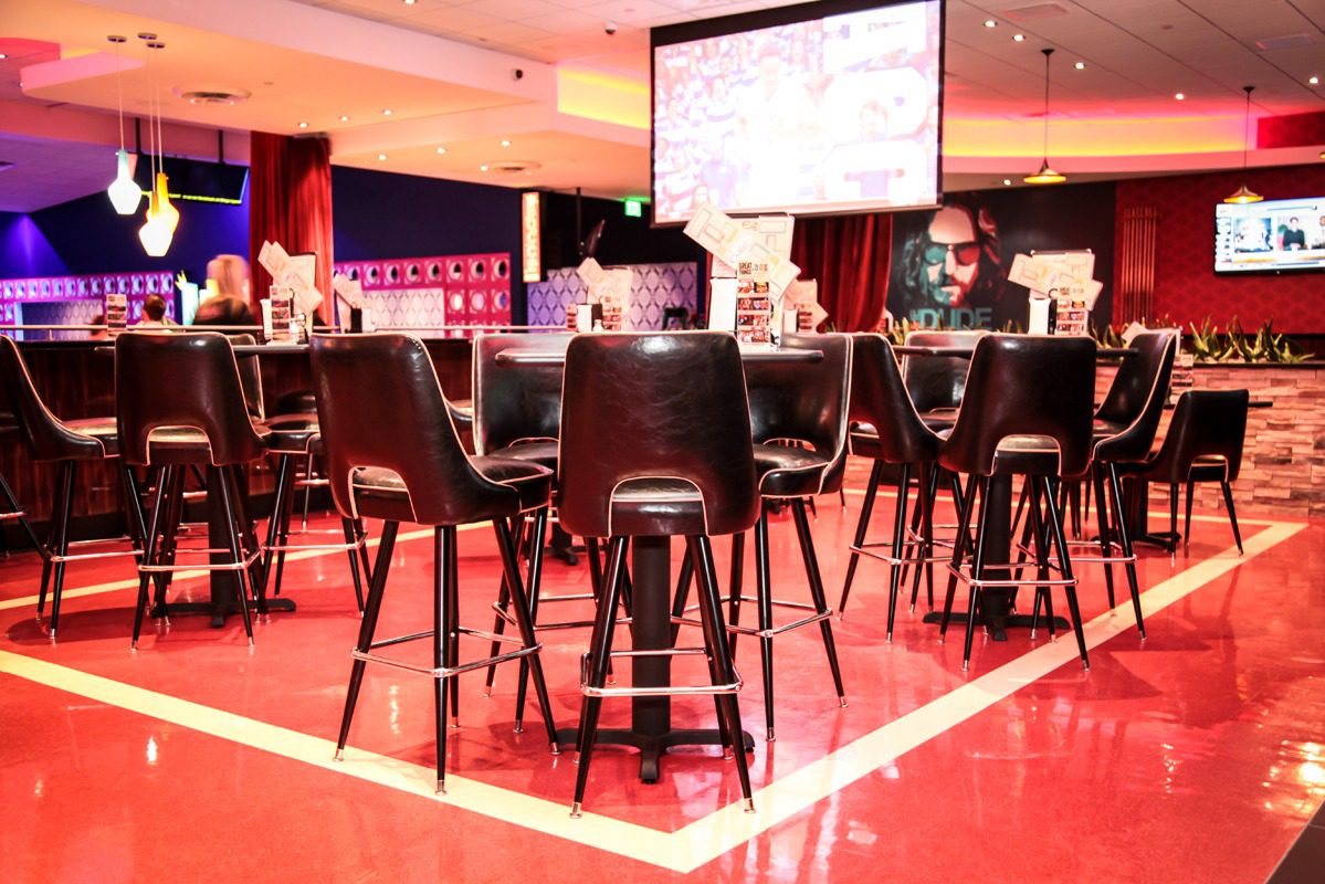 Modern bar area with high stools and a large screen in a dimly lit setting.