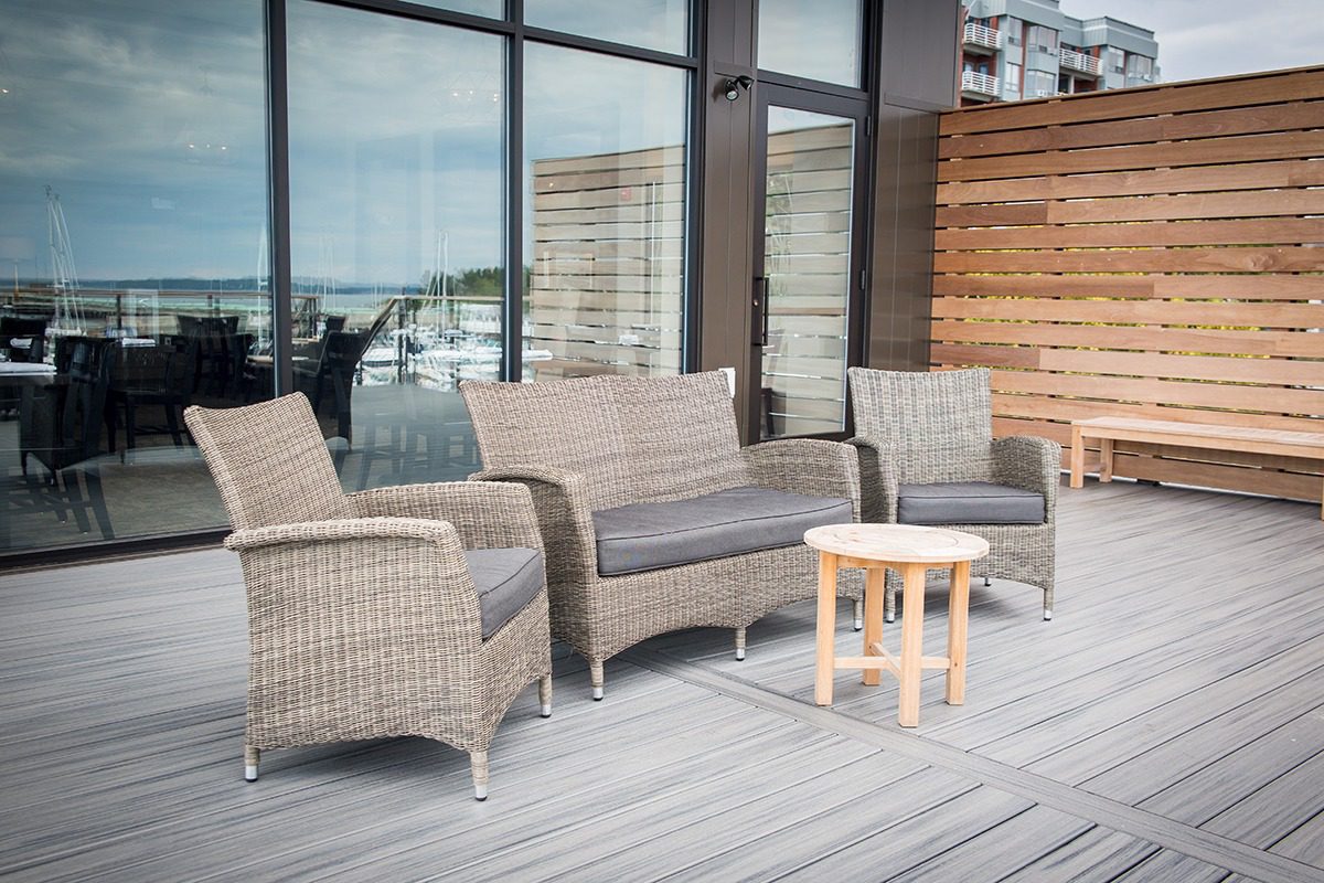 Modern outdoor wicker furniture set on a wooden deck with glass walls.