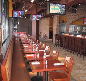 Empty restaurant with wooden tables and chairs, and multiple TVs.