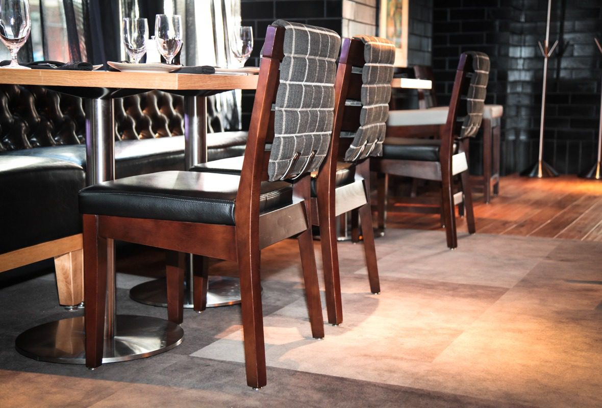 Wooden chairs with black cushions lined up in a dining area.