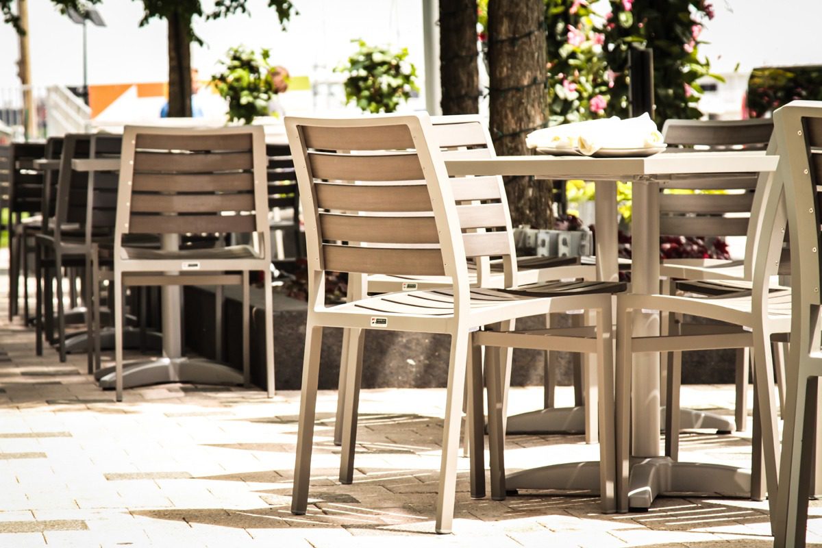 Empty outdoor wooden chairs and tables on a sunlit patio.