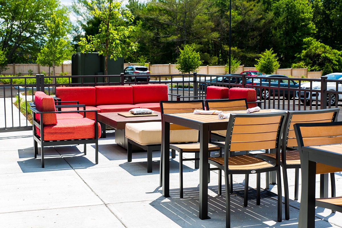 Modern outdoor seating area with red couches and wooden tables on a sunny day.