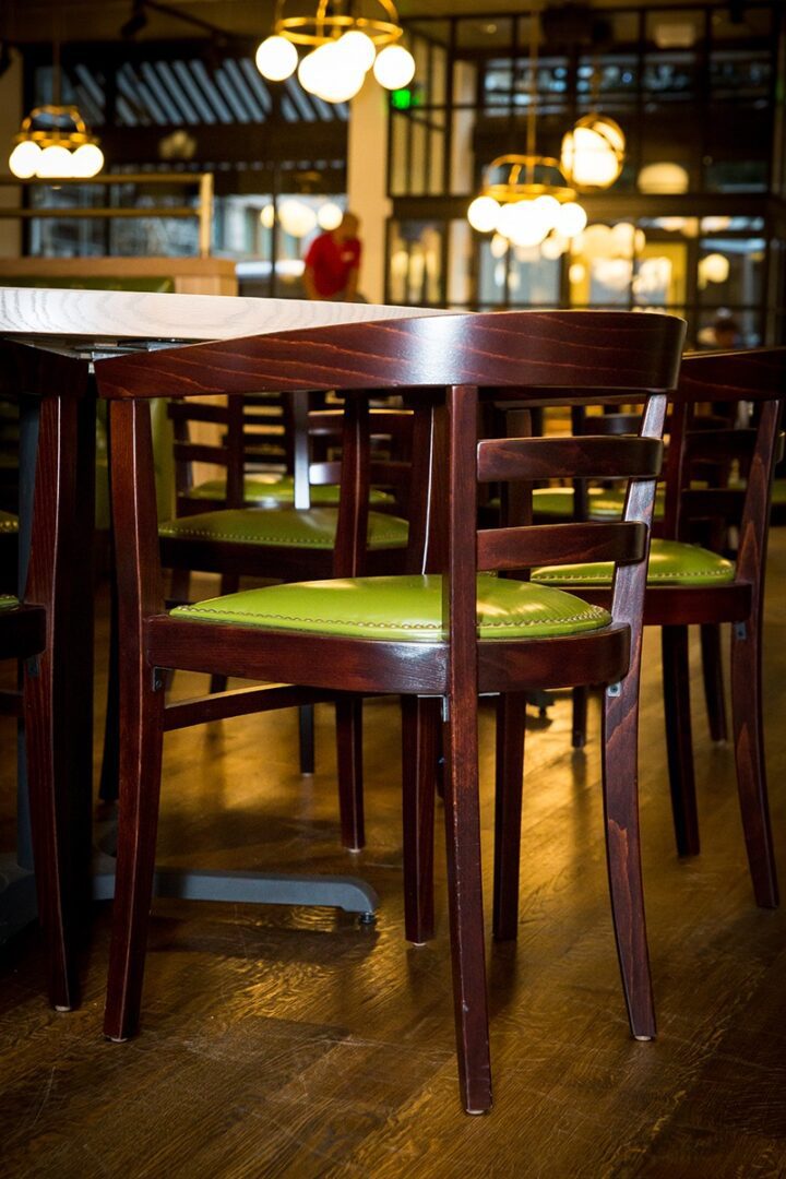 Wooden chairs with green cushions around a dining table in a cozy restaurant.