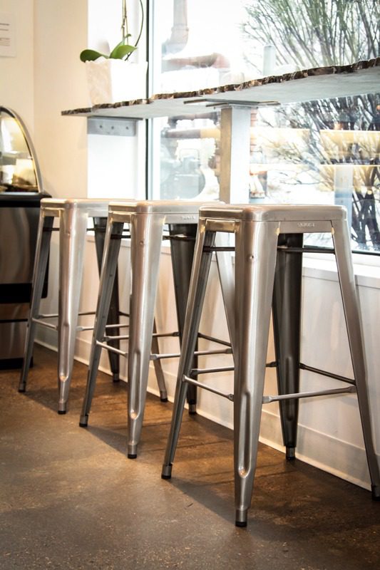 Metal bar stools lined up by a window in a bright cafe.