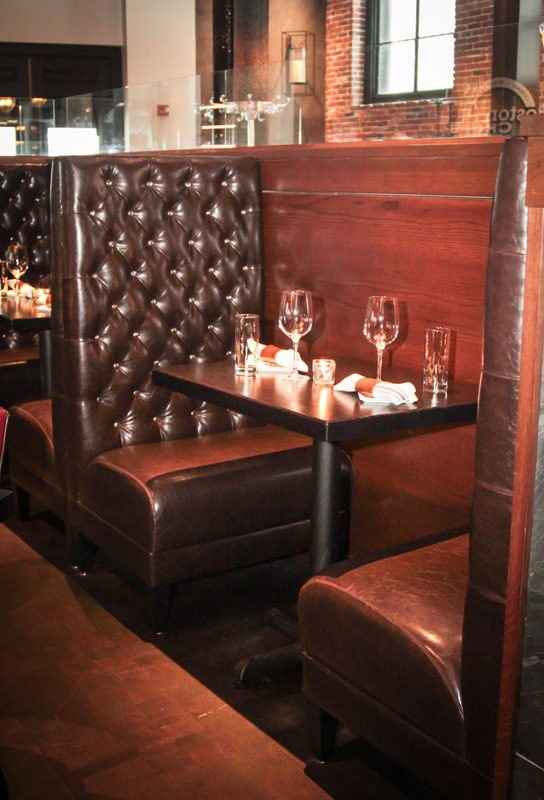 Cozy leather booth seating with wine glasses on a wooden table in a rustic setting.