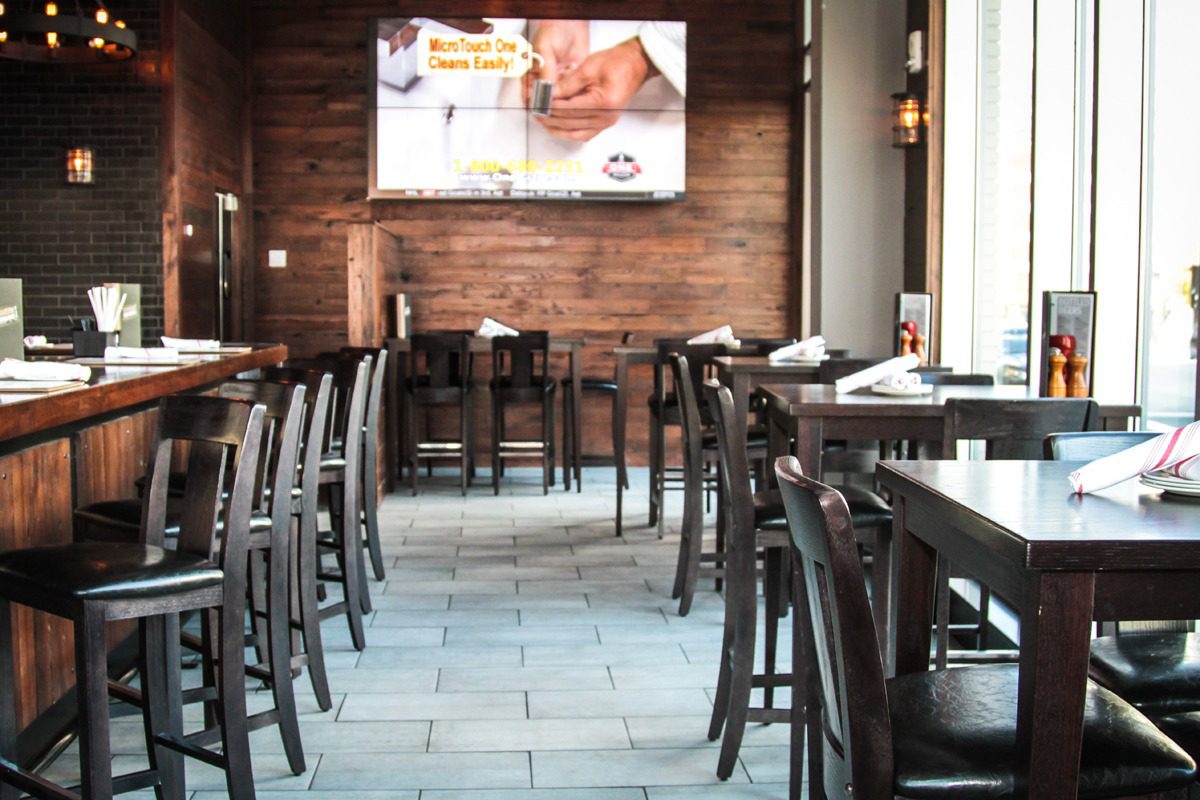 Empty wooden chairs and tables in a cozy restaurant with a large menu board.