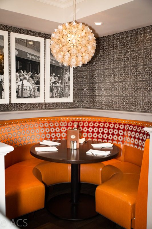 Cozy round booth with orange seating and a chandelier in a modern restaurant.