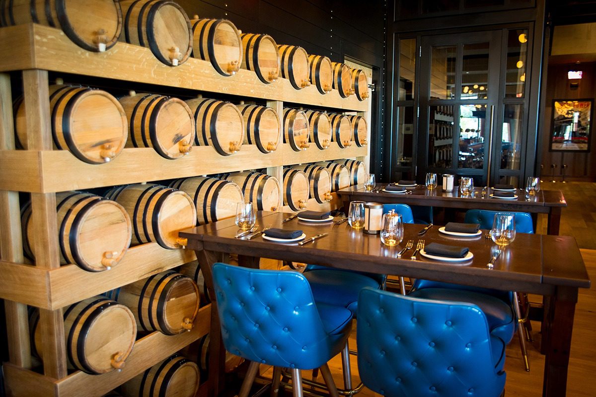 Cozy dining area with blue chairs and wooden barrels stacked on shelves.