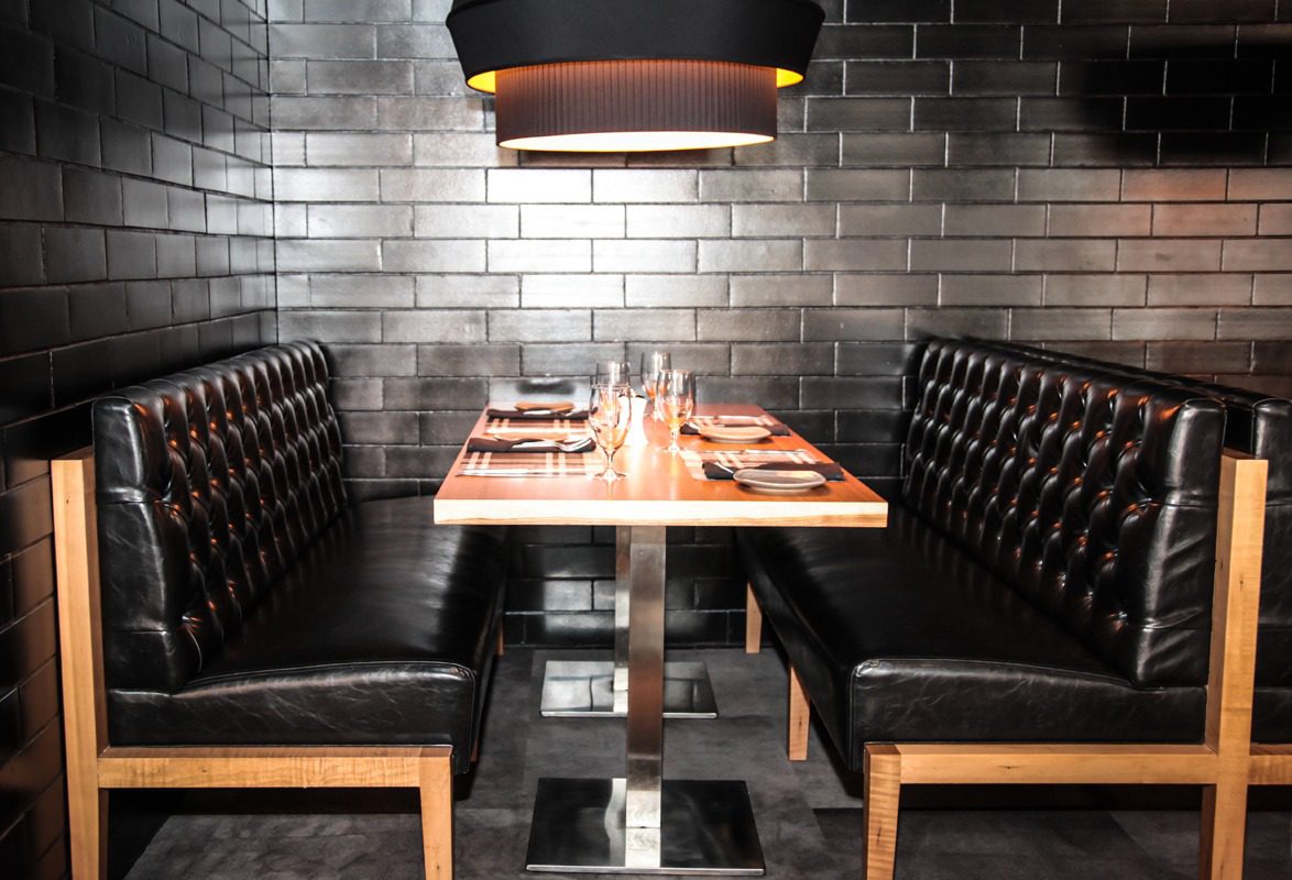 Cozy restaurant booth with modern black leather seating and wooden table.