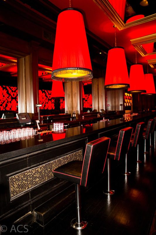 A stylish bar interior with red pendant lights and black chairs.