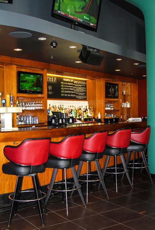 Cozy bar with wooden counter and red cushioned stools.