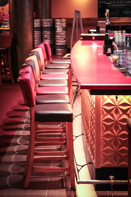 Row of red bar stools lined up at a glowing bar counter.