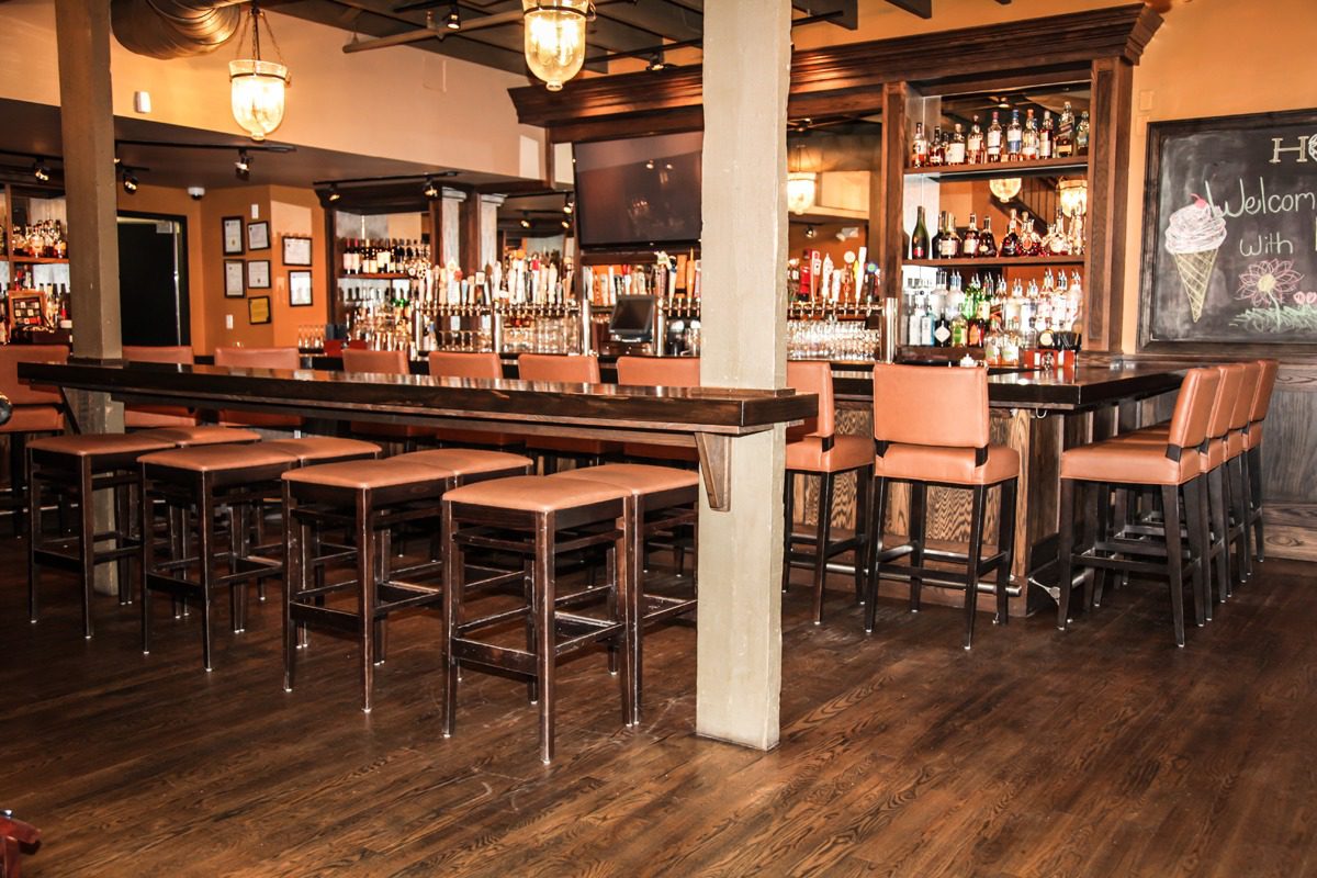 Cozy bar with wooden stools, tables, and warm lighting.