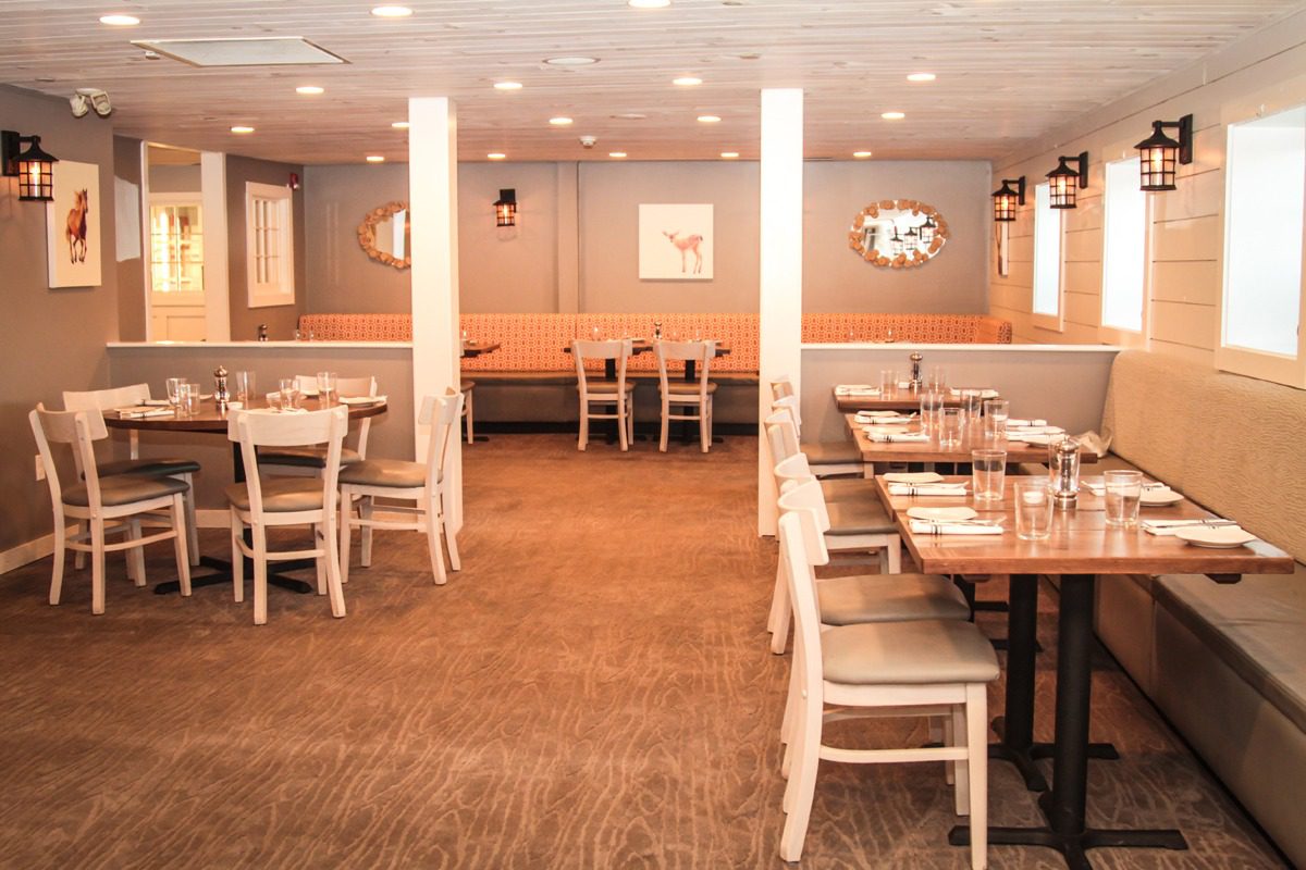 Cozy, well-lit dining area with wooden chairs and tables set for guests.