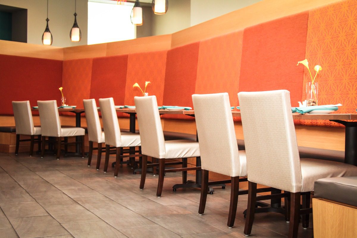 Modern restaurant dining area with white chairs and warm orange walls.