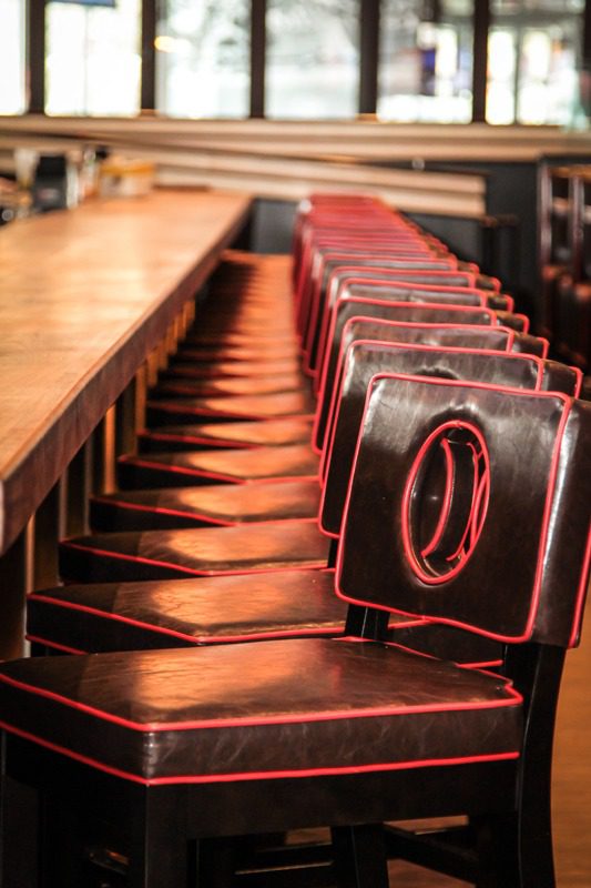 Empty bar stools lined up along a wooden counter in a dimly lit setting.