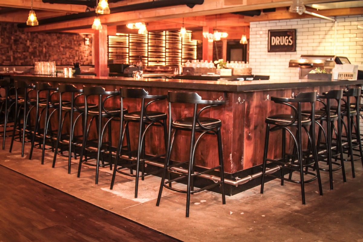 Cozy bar with wooden stools and warm lighting.