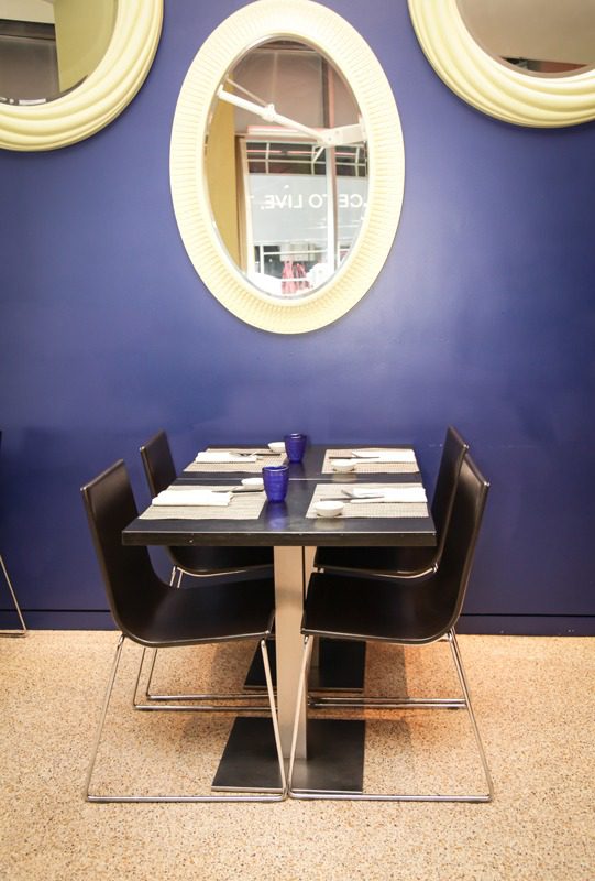 Cozy dining table set for four with a purple wall and oval mirror.